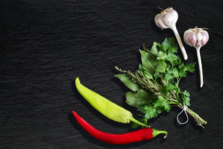 Bouquet garni and spicy vegetables. Bay leaf, parsley and thyme, bound with culinary thread, chili pepper and garlic on slate backgroundの写真素材