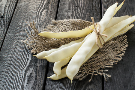 Bunch of white string beans tied with twine. Long white pods on sackcloth on dark wooden table. New...