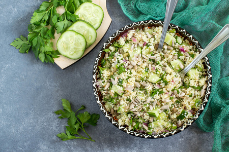 Bowl with couscous, cucumber, parsley, sunflower seeds and sesame on gray background with yellow napkin. Vegetable ingredients on table. Dietary and healthy food. Top viewの写真素材