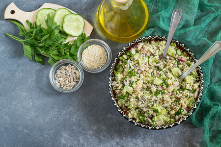 Bowl with couscous, cucumber, parsley, sunflower seeds and sesame on gray background with green napkin. Dietary and healthy food. Top viewの写真素材