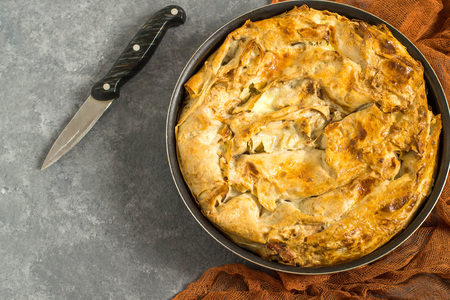 Simple homemade pie made of puff pastry with cheese and herbs. Pan with pie on rufous gauze napkin...
