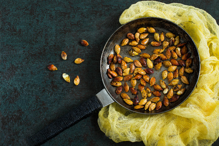 Pumpkin seeds fried with spices on old iron frying pan. Dark textured background, yellow gauze napkin. Rustic styleの写真素材