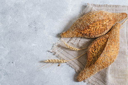 Whole wheat bread with flaxseeds and ears of wheat on linen napkin. Useful dietary bread without yeast. Gray textured backgroundの写真素材