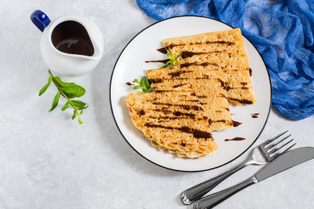 Thin russian pancakes with chocolate sauce. Prepare for holiday Maslenitsa in honor of end of winter. Pancakes on plate, chocolate sauce in gravy boat, mint, on light gray backgroundの写真素材