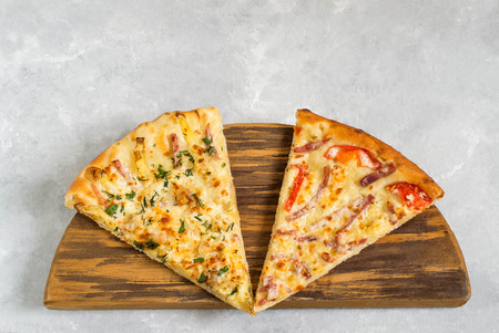 Two different pieces of delicious pizza on wooden board on light gray stone backgroundの写真素材