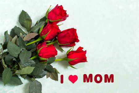 Bouquet of red roses and inscription: I love mom on light green background. Congratulations on Mother's Dayの写真素材