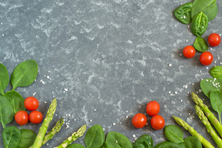 Fresh organic vegetables: asparagus, spinach and cherry tomatoes. Frame of vegetables and sea salt on gray background. Healthy food, vegetarian dieting concept の写真素材
