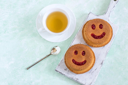 Funny cupcakes in form of smiling face and cup of tea. Food that causes positive emotions. Humorous sweet food. Good mood. Delicious homemade pastriesの写真素材