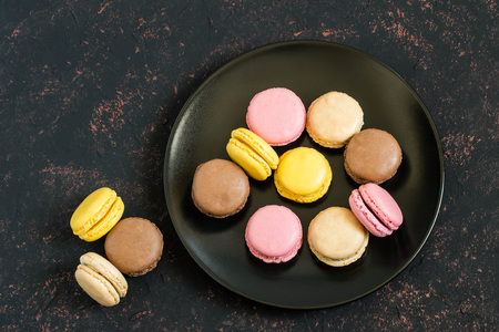 Different macaroon on black plate on dark background. Delicious and sweet almond cookies macaroon with cream, French delicacy. Colorful texturesの写真素材