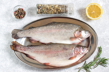 Two fresh trout on metal tray and ingredients for cooking (pepper, salt, lemon, seasoning and...