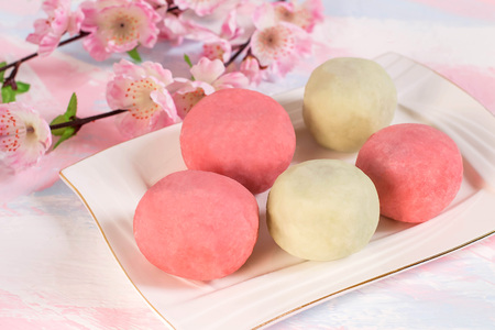 Multicolored daifuku mochi stuffed with sweet bean paste and strawberry on plate, cup of tea and...