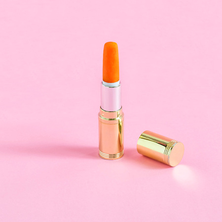 Tube of lipstick and mini carrot on pastel pink background. Minimalistic style. Creative idea of color and shape. Fantasies on theme of food and fashionの写真素材
