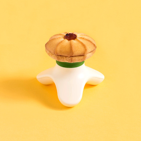 Compact massager and shortbread on yellow background. Minimalist style. Creative idea, imagination and fantasy. Attraction of attention to problems of physical inactivity and abuse of sweetの写真素材