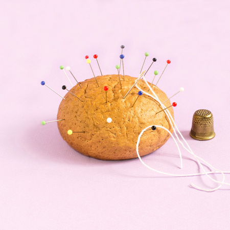 Bun like needle bed and thimble on pastel pink background. Minimalistic style. Creative idea,...