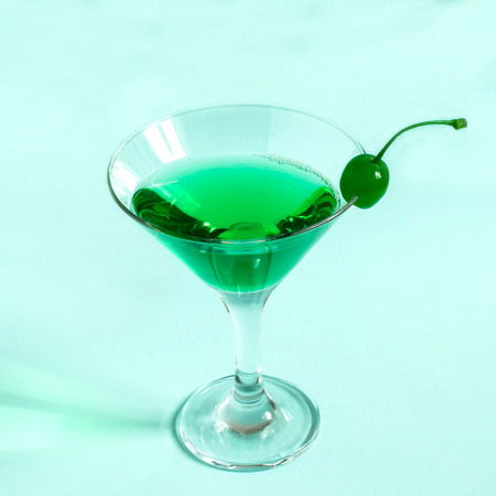 Green cocktail with maraschino cherry in martini glass on pastel blue background. Minimal style. Concept of bright original drinksの写真素材