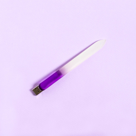 Nail file with USB flash drive on lilac background. Creative idea, imagination and fantasy. Minimal style. Humorous concept of nail care in workplace at computerの写真素材