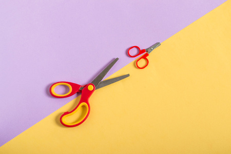 Small and large scissors with red handles on two-color paper background of lilac and yellow. Minimal style. Concept of education: from small to large, from simple to complexの写真素材