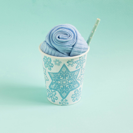 Socks in paper cup, hand-decorated with applique of snowflakes on blue background. Imitation of festive cocktail. Minimal style. Creative idea, imagination and fantasy. Christmas and New Year conceptの写真素材
