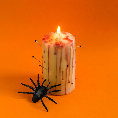 Homemade decor for Halloween. Candle pierced with needles with red brooks and drops like blood and spider on orange background. Minimal style. Original designの写真素材