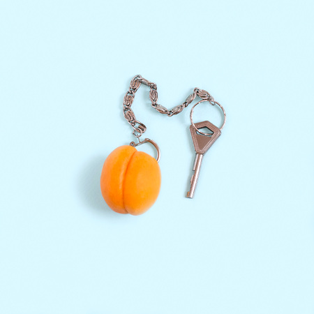 Apricot as keychain with key on pastel blue background. Minimal style. Creative idea, imagination and fantasy. Original food concept: fruit is key to diet and healthy eatingの写真素材