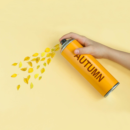 Yellow leaves fly from spray can with inscription: autumn. Yellow pastel paper background. Minimal...