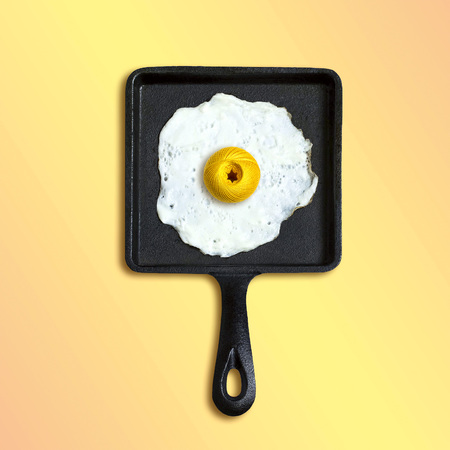 Square cast-iron frying pan with fried eggs, ball of yarn instead of yolk. Artificial objects that mimic natural forms. Creative idea, imagination and fantasy. Original minimal conceptの写真素材