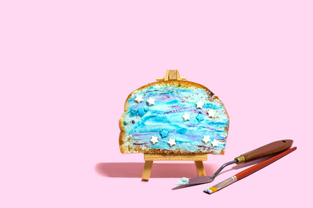 Toast with colored ricotta and sugar decoration on easel, spatula and brush. Imitation of picture. Creative idea, imagination and fantasy. Minimal style. Original food conceptの写真素材