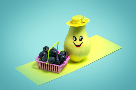 Fruits like people. Pear in hat bought basket of grapes. Light blue backgroundの写真素材