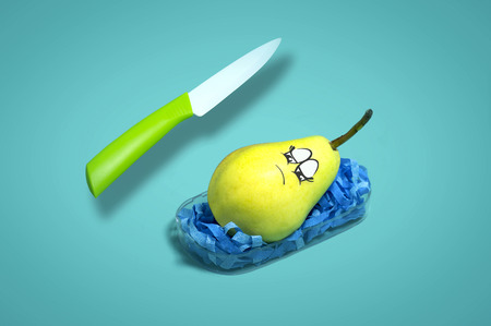 Fruits like people. Pear has nightmare about knife attack. Light blue paper backgroundの写真素材