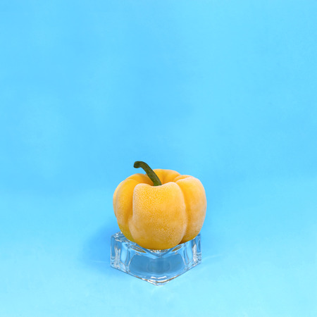 Frozen yellow pepper on ice cube on blue background. Creative concept: quickly frozen fruits and...