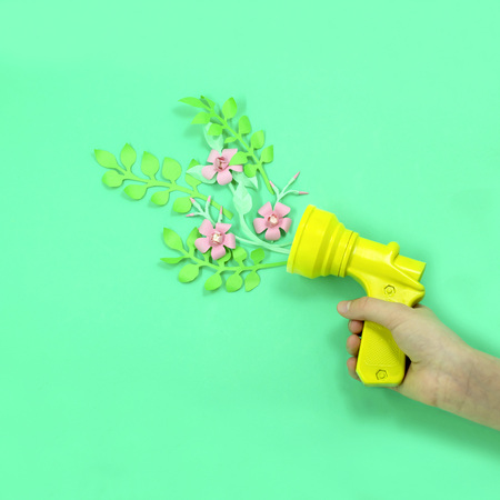 Culinary pistol in woman's hand shoots paper flowers. Beautiful holiday card for Valentine's Day, Women's Day, Mother's Day. Paper art and paper craft. Minimal styleの写真素材