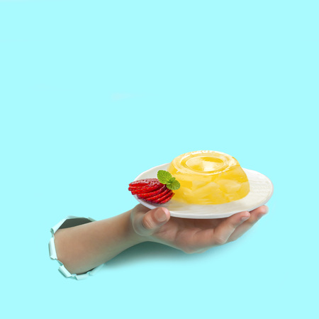 Hand is holding plate of pineapple jelly and pieces of fresh strawberries through torn paper. Minimum summer food conceptの写真素材