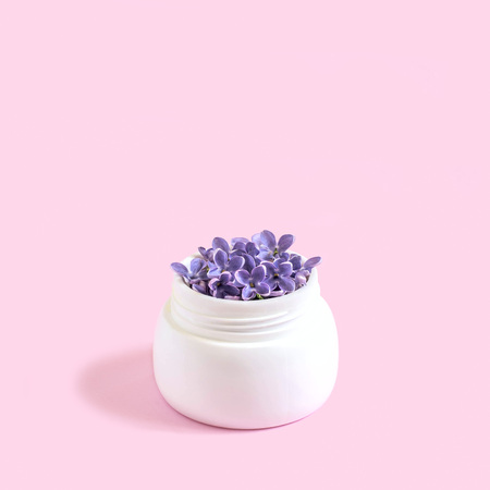 Jar with flowers of lilac as cosmetic cream on pastel pink background. Minimalist style. Creative idea, imagination and fantasy. Concept of natural cosmeticsの写真素材