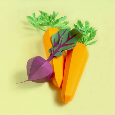Colorful volumetric carrot and beet made from paper on yellow background. Paper art and craft. Trendy hobby. Creative, vegetarian, healthy or food art conceptの写真素材