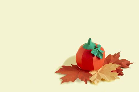 Paper pumpkin and autumn leaves on yellow background. Paper art and craft. Trendy hobby. Autumn food art concept. Copy spaceの写真素材