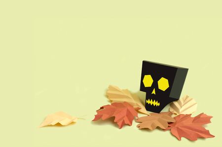 Volumetric paper skull with autumn leaves on yellow background. Paper art and craft. Festive Halloween concept. Copy spaceの写真素材