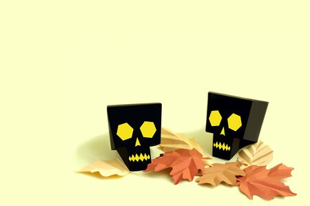 Volumetric paper skulls with autumn leaves on yellow background. Paper art and craft. Festive Halloween concept. Copy spaceの写真素材