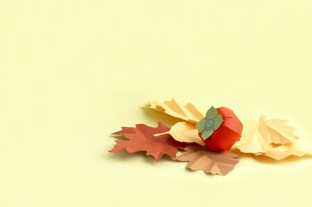 Paper persimmon and autumn leaves on yellow background. Paper art and craft. Trendy hobby. Autumn food art concept. Copy spaceの写真素材