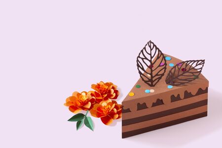 Piece of paper chocolate cake and flowers. Cake is decorated with paper chocolate leaves. Volumetric handmade paper objects. Paper art and craft. Trendy hobby. Minimal art food concept. Copy spaceの写真素材