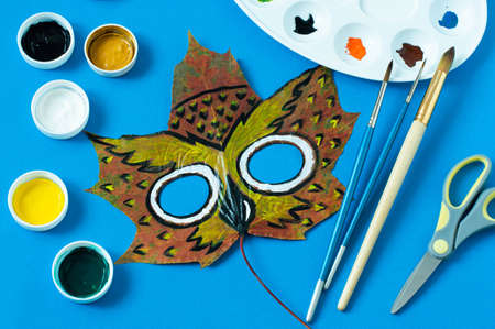 Mask painted on maple leaf. Drawing on autumn leaves. Owl mask for kids autumn carnival or party. Art project for children. DIY conceptの写真素材