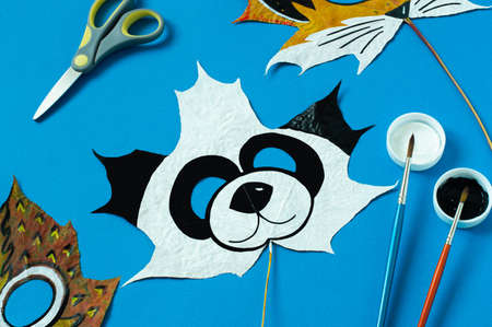 Mask painted on maple leaf. Drawing on autumn leaves. Panda mask for kids autumn carnival or party. Art project for children. DIY conceptの写真素材