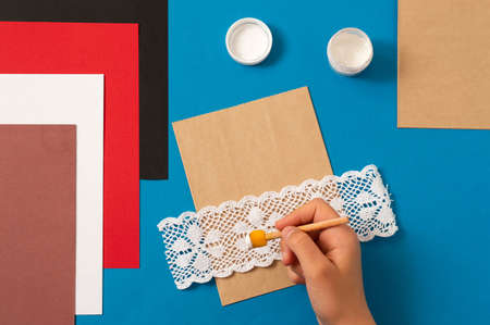 Child decorates craft gift bags for Christmas. Original project for children. DIY concept. Step-by-step photo instructions. Step 2. Make an imprint with laceの写真素材