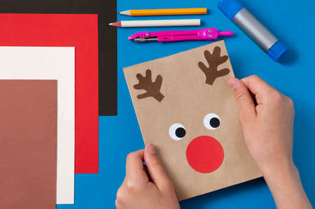 Child decorates craft gift bags for Christmas. Original project for children. DIY concept. Step-by-step photo instructions. Step 8. Glue details of deer's faceの写真素材