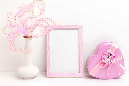 Photo frame mockup with pink fluffy decorative plant in vase and pink heart-shaped gift box on white backgroundの写真素材
