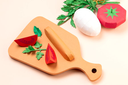 Ingredients for making scrambled eggs. Tomato, egg and parsley on table. Tomato slices and sausage on cutting board. Real volumetric handmade paper objects. Paper art and craftの写真素材