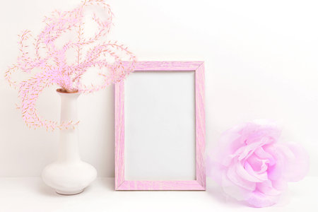 Photo frame mockup with pink fluffy plant in vase and decorative silk rose on white backgroundの写真素材