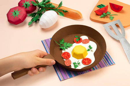 Realistic paper fried eggs with tomatoes and sausage in frying pan. Ingredients for fried eggs on table. Real volumetric handmade paper objects. Paper art and craftの写真素材