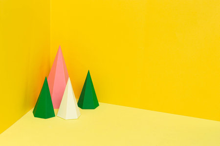 Multi-colored hexagonal paper pyramids stand in corner on yellow background. Paper art and craft