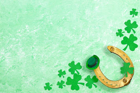 Golden horseshoe, clover shamrocks, green hat on green textured background. Festive background for St. Patrick's Day. Copy spaceの写真素材