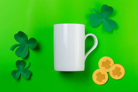 St. Patrick's Day empty white mug mockup. White coffee mug, paper clover shamrocks and coins on green backgroundの写真素材